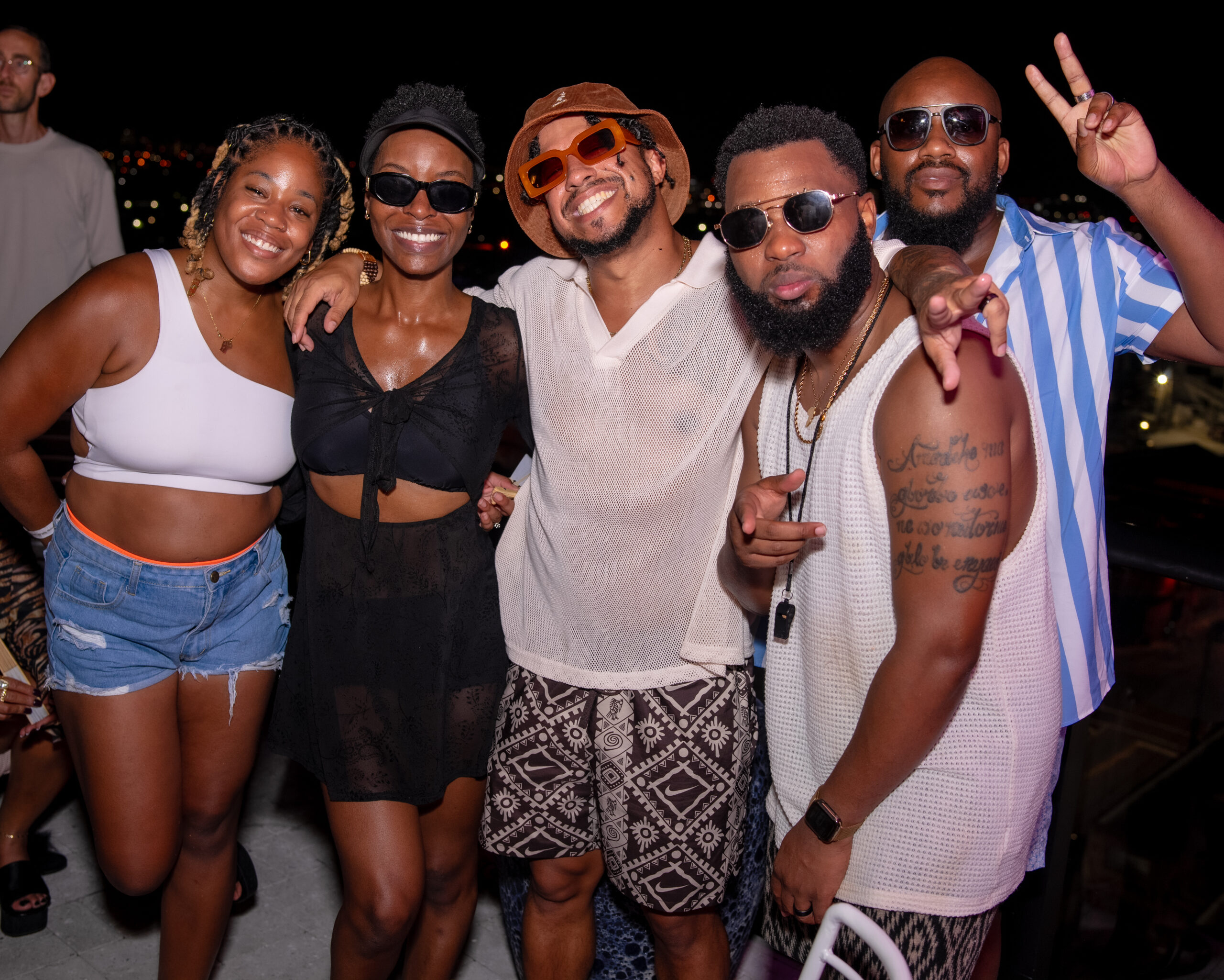 Five people are posing and smiling at a nighttime outdoor event, with city lights in the background.